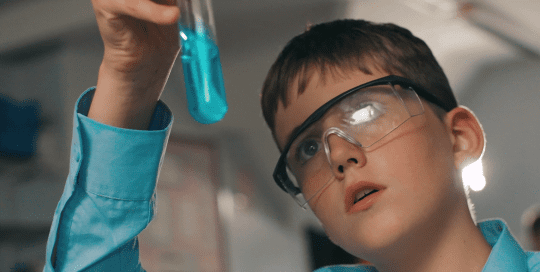 A boy holds up a test tube with bright blue liquid.