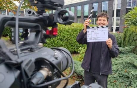A Smiling Man Posing With A Clapperboard On A Corporate Video Production.