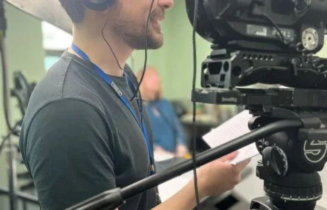 Video Production On Site In An Office. A Camera Operator Talks To The Interviewee Off Camera.