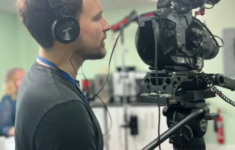 Video Production On Site In An Office. A Camera Operator Talks To The Interviewee Off Camera.