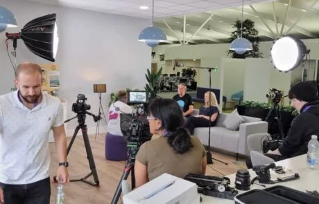 A Group Of People Sitting In A Room With A Camera