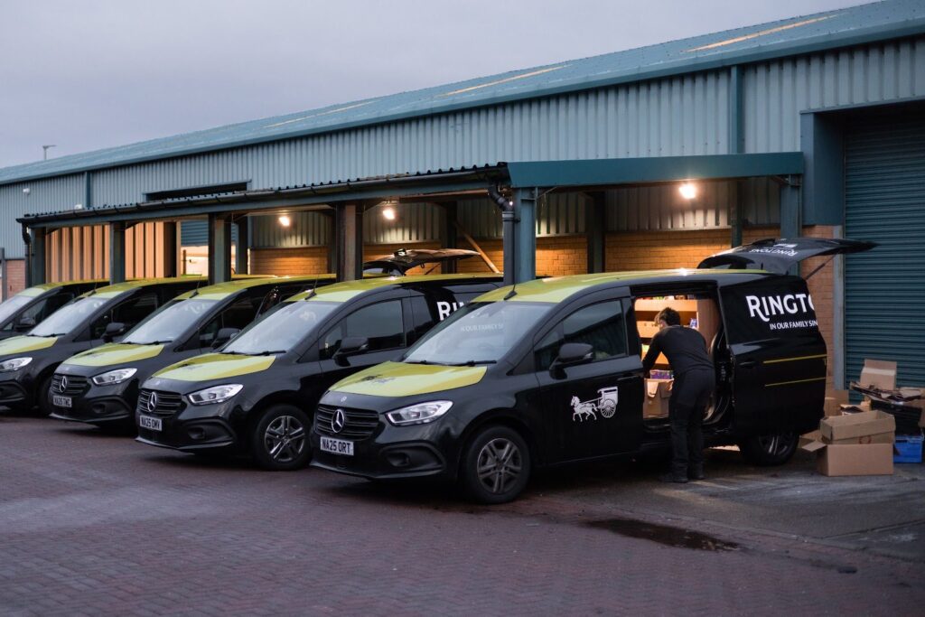 Ringtons delivery vans lined up at dusk, one being loaded