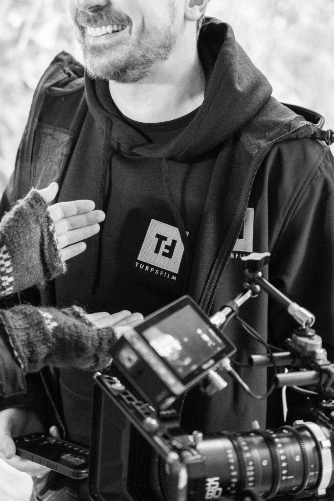 Turps Film crew member holding a cinema camera rig, wearing a branded Turps Film hoodie
